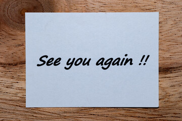 The words "See you again" are written on a piece of white paper on a wooden table.