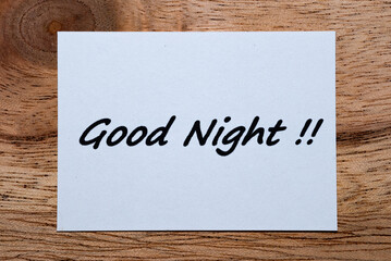 The words "Good Night" are written on a piece of white paper on a wooden table.