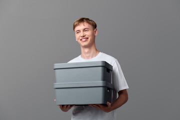 Delivery, man, carrying two gray storage boxes for shipment, casual attire and studio setup, emphasizing moving, packaging, and logistics. Clean background highlights handling goods and readiness for