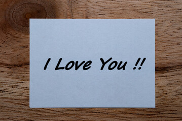 The words I Love You written on a piece of white paper on a wooden table.