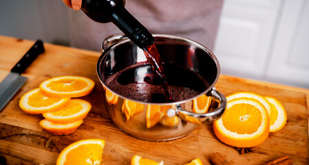 Woman adding cinnamon stick to mulled wine pot in festive Xmas or New Year kitchen preparing warm...