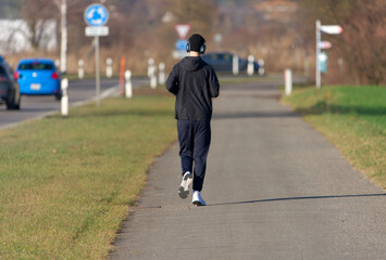 Rear view of young man with cap and headphones at Swiss village of Niederglatt on a sunny autumn afternoon. Photo taken December 20th, 2025, Niederglatt, Canton of Zurich, Switzerland.