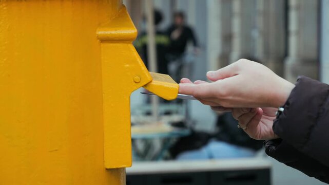 A woman's hand drops a postcard into a mailbox. A person sends an envelope with postcard and puts it in the yellow mailbox on the street. High quality 4k footage