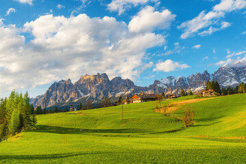View of Cortina d'Ampezzo with lush green field, wooden houses and snow covered Dolomiti Alps mountains. Italian Dolomites landscape in Belluno region, Italy. Travel and touristic destination