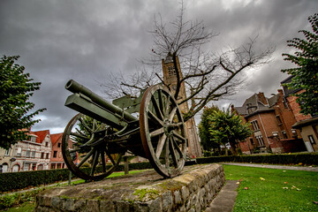 Remains of european military history in belgian village of Warneton, former battlefield site.  WWI artillery cannon war memorial with church tower and dramatic sky. 