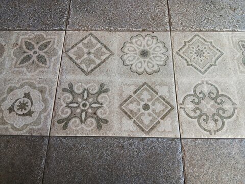 Close up abstract texture of grey and off white encaustic style cement or hydraulic tiles with geometric and floral patterns.