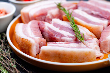 Pork belly pieces arranged on a plate with herbs in a kitchen setting ready for cooking