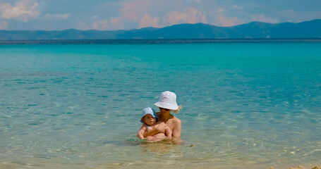 Nurturing mother cradling infant in tranquil turquoise waters, experiencing peaceful maternal bonding during serene seaside vacation moment