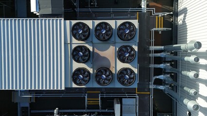 Aerial drone top down rotating view of cooling and ventilation systems on a data storage center warehouse building showing modern infrastructure. © Liam Carter
