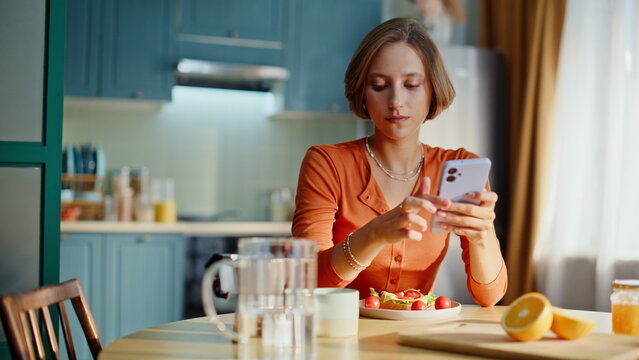 Relaxed woman enjoy breakfast looking cellphone screen at home kitchen closeup.
