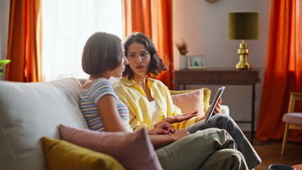 Relaxed besties shopping online browsing tablet on couch modern living room. 