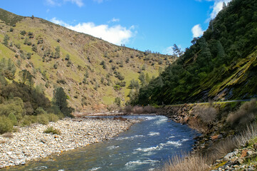 Scenic river flows through a mountainous valley under a bright blue sky, showcasing nature's beauty in a serene landscape.