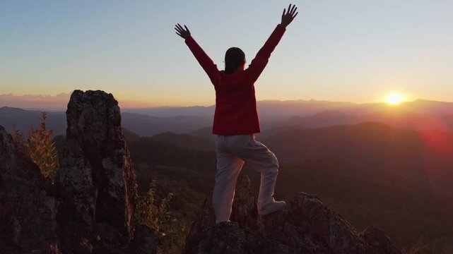 Silhouette of a person feeling strong and empowered, standing tall on the top of a mountain at sunrise