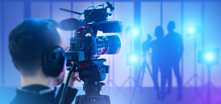 Video production filming process led by a camera operator recording people under studio lights. Media production, broadcasting, content creation, cinematography, and event coverage.