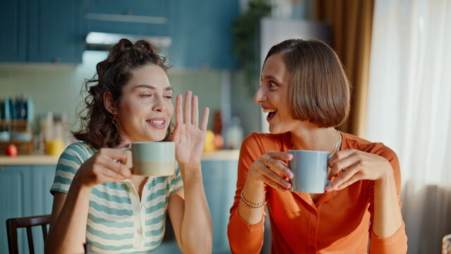 Two sisters gossiping kitchen holding coffee cups closeup. Happy women friends
