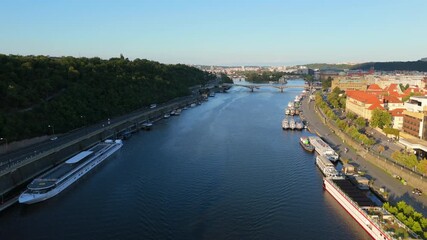 Dynamic cinematic aerial shot capturing Vltava River, passing boats and sunlit riverside scenery in Prague Czech Republic, revealing wide city perspective and calm morning movement