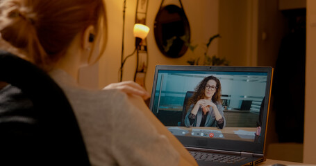 Two women engage in a collaborative business discussion through a laptop video call while working from home in a cozy office environment.