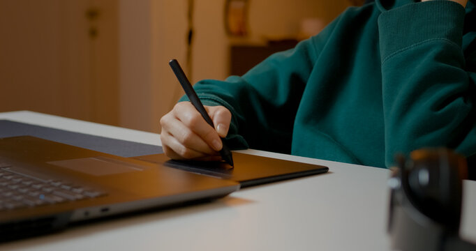 Female graphic designer focusing intently on photo retouching, using graphics tablet while working comfortably from home studio during evening hours