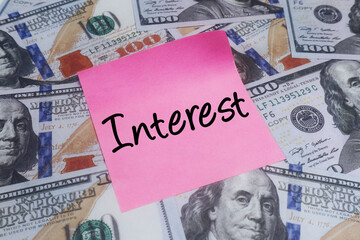 Pink sticky note with INTEREST text over US dollar bills. Concept of financial growth, banking and investment.