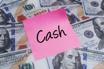 Pink sticky note with CASH text over US dollar bills. Concept of liquidity, physical currency and payment.