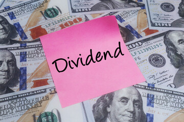 Pink sticky note with DIVIDEND text over US dollar bills. Concept of investment returns and corporate profit.