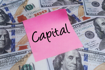 Pink sticky note with CAPITAL text over US dollar bills. Concept of financial investment, wealth and funding.