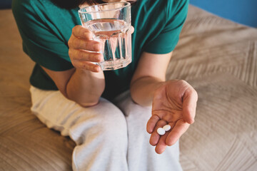 Woman taking medication, holding medicine pills and glass of water