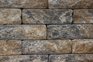 Naklejka premium Textured stone wall made of rectangular blocks in earthy tones, showcasing natural variations and patterns, ideal for backgrounds and architectural designs with copy space