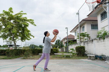 Active woman playing basketball on a village court, dribbling and shooting in natural outdoor light, capturing healthy lifestyle, community sports, energetic athletic movement action.