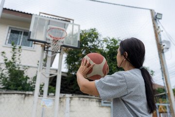 Active woman playing basketball on a village court, dribbling and shooting in natural outdoor light, expressing healthy lifestyle, community sports, fitness activity, energetic motion.