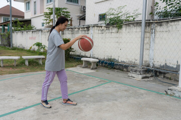 Energetic woman practicing basketball outdoors on a village court, dribbling and shooting in daylight, showing active lifestyle, community recreation, physical fitness, youth sports culture.