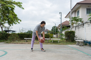 Young woman playing basketball on an outdoor village court, dribbling and shooting with focus, highlighting healthy living, community sports activities, natural light, physical strength.