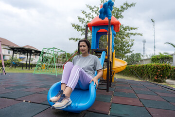 A woman sitting on a children&rsquo;s slide at a neighborhood park, enjoying a calm outdoor moment, reflecting leisure time, community space, casual lifestyle, urban recreation, and relaxed everyday living.