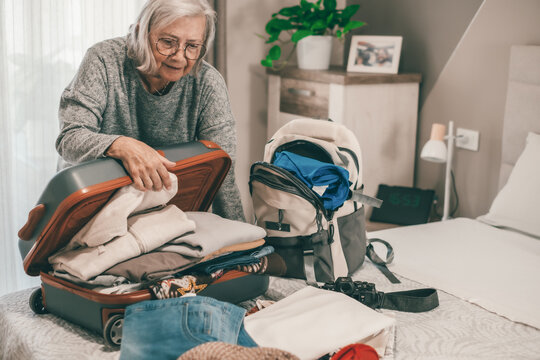 Full suitcase concept, stressed senior woman in bedroom packing, preparing luggage case of clothes. Concept of travel anxiety, forgetting items, senior lifestyle, vacation preparation
