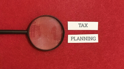 Magnifying glass examining the words TAX PLANNING on a textured red background, symbolizing financial analysis and strategy