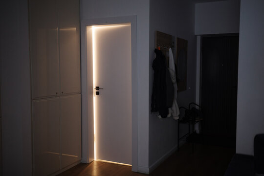 Glowing light shining through the edges of a closed white door in a dark interior hallway.