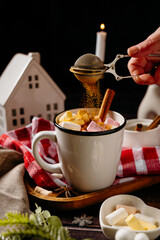 Hands adding topping to hot cocoa with marshmallows on cozy winter table. Warm holiday drink preparation and home comfort lifestyle moment.