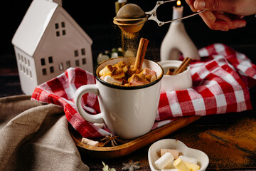 Hands adding topping to hot winter drink with cookies and festive decor. Cozy holiday cooking moment and home comfort lifestyle.