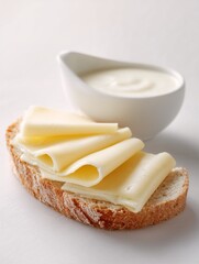 Slices of cheese on rustic bread with bowl of cream on white background