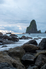 Fototapeta premium Mystical seascape with dark volcanic rocks and tall sea stacks emerging from silky ocean water during twilight, showcasing serene coastal nature.