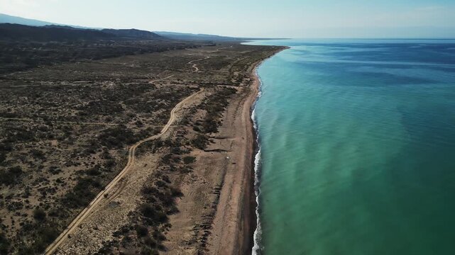 Aerial view of white tents nestled between the azure waters of the lake and the rugged, sun-drenched mountains, Ak Say, Issyk-Kul Region, Kyrgyzstan