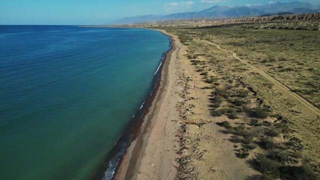 Aerial view of white tents nestled between the azure waters of the lake and the rugged, sun-drenched mountains, Ak Say, Issyk-Kul Region, Kyrgyzstan
