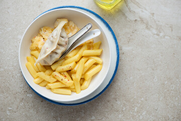 Bowl of cheesy tteokbokki or rice cakes with steamed egg and dumpling, horizontal shot on a beige stone background with space, flat lay