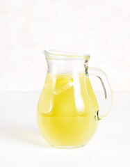 Lemon lemonade in glass pitcher on light background