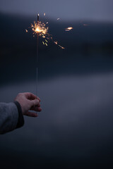 A hand holds burning sparkler in the evening dusk. Vertical background for christmas and new year's...