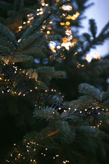 Vertical close-up of a christmas tree with golden bokeh lights.