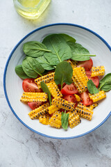Plate of tomato, fresh spinach and grilled corn salad on a white stone background, vertical shot, elevated view