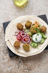 Wheat wraps with falafel, vegetables and white yogurt on a beige granite background, vertical shot, selective focus