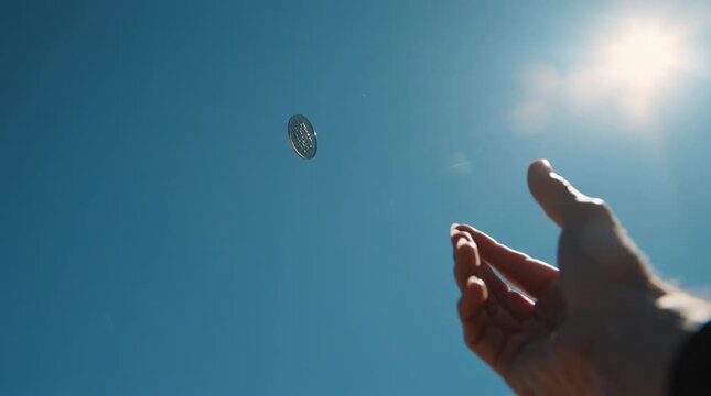 Coin in the Air: An individual extends a hand towards a coin suspended mid-air against a vibrant blue sky, inviting a sense of chance and anticipation. 