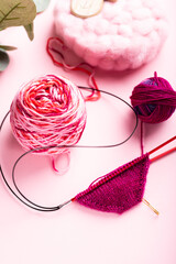 Vibrant yarn balls in pink and red hues, knitting needles with a small knitted piece, surrounded by soft materials, illustrating the joy of knitting and crafting